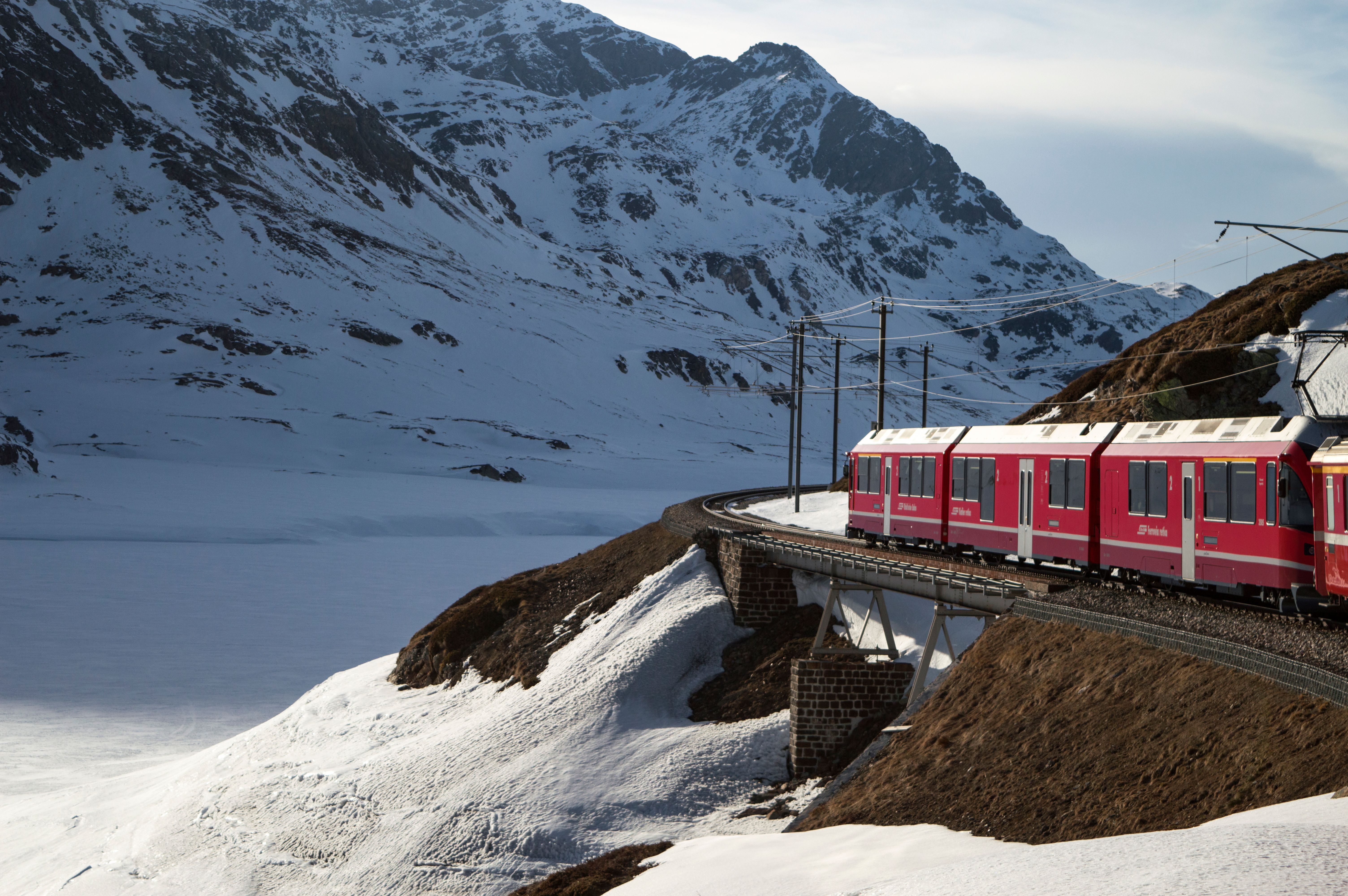 Red train curving beside snowy mountains in the Swiss Alps