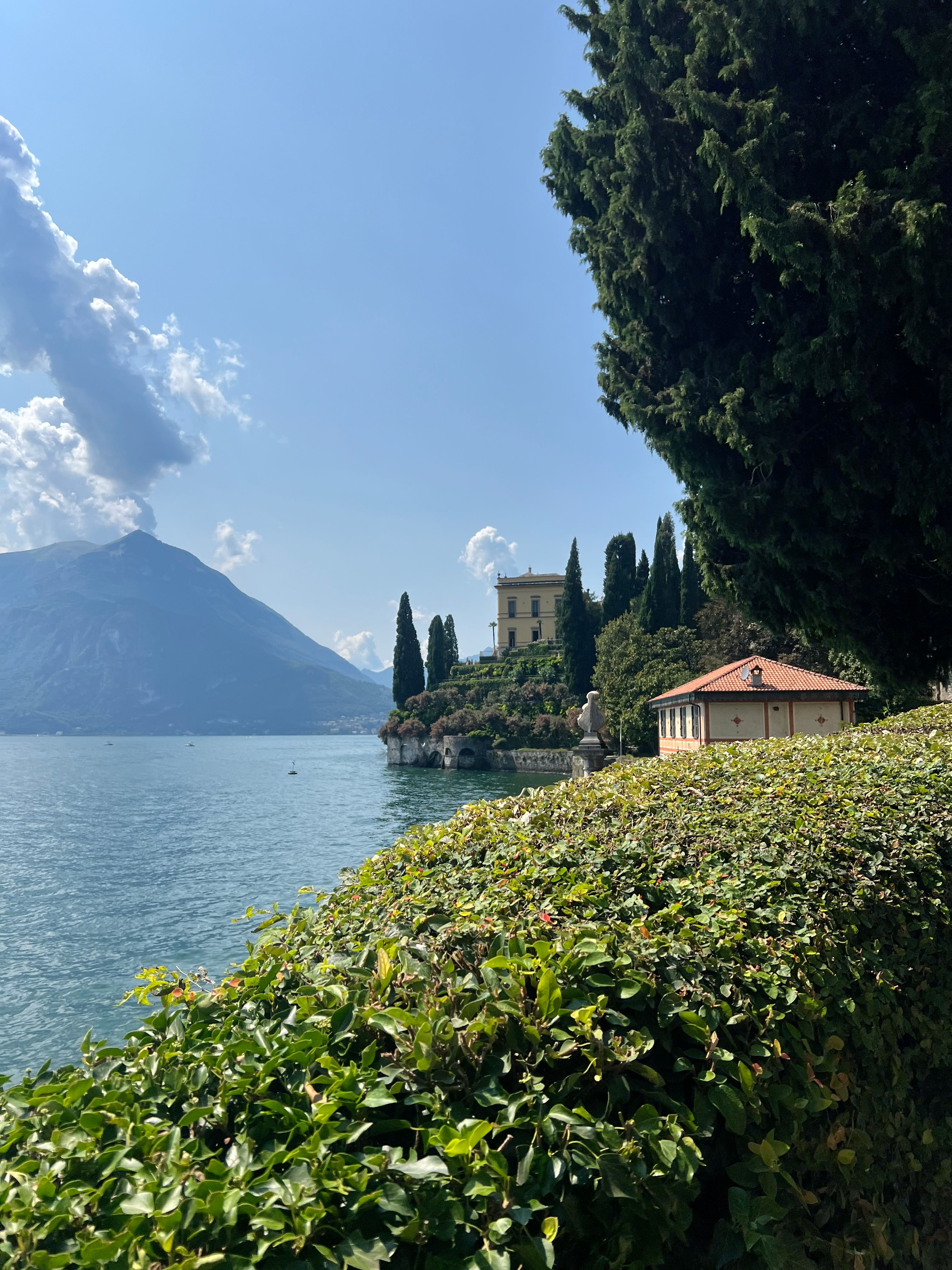Lake Como with blue water, mountains, lakeside buildings and green gardens